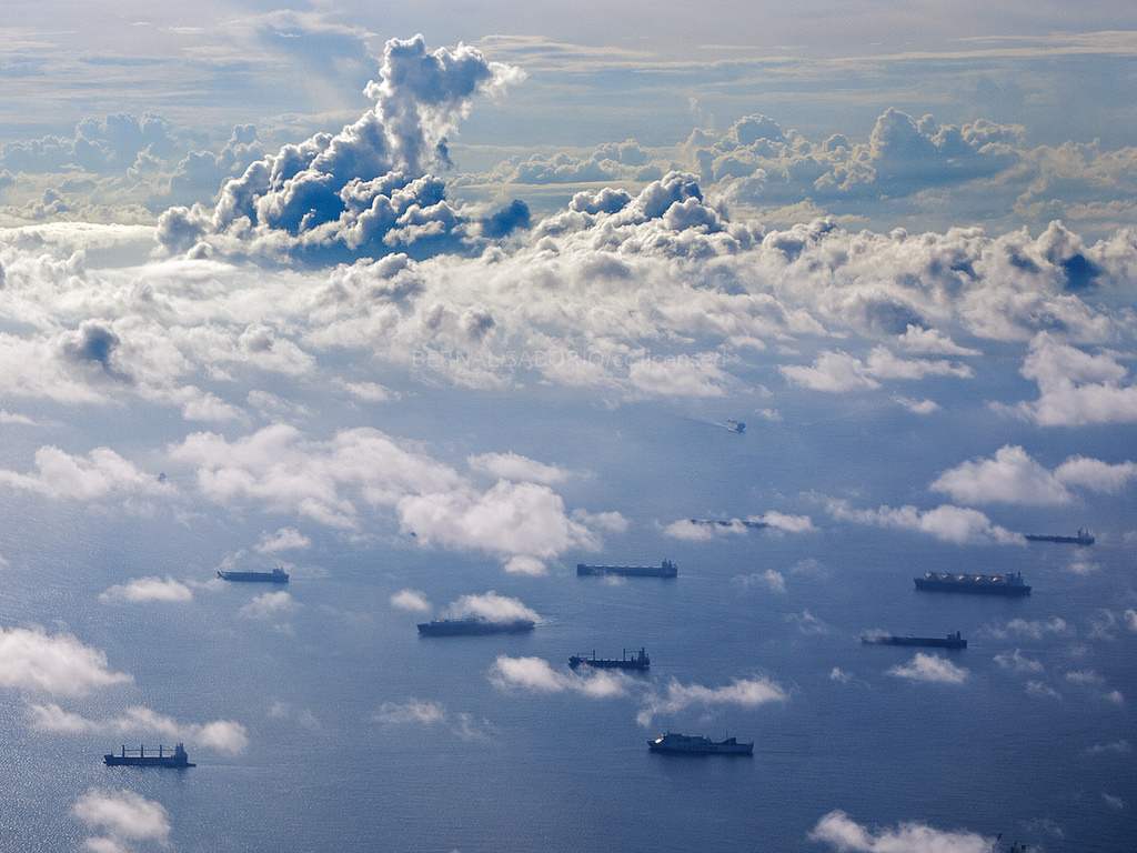 Ships traverse an azure sea while white clouds billow and swell overhead.