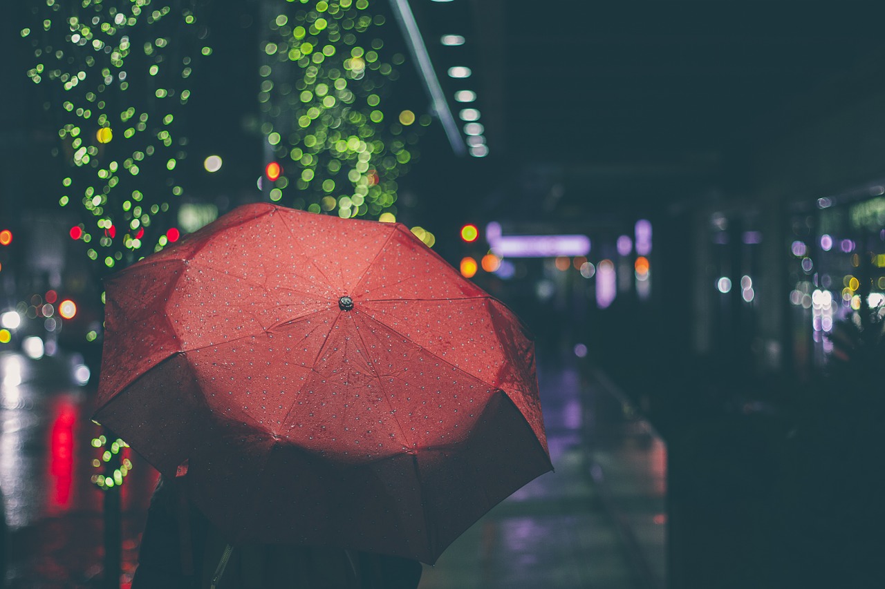 Red umbrella against a rainy city background at night