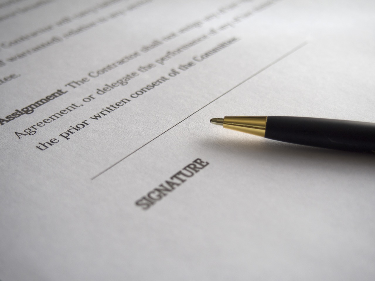 Legal document on white paper with words suggesting a contract, line for a signature, with a black ball point pen laying across it.