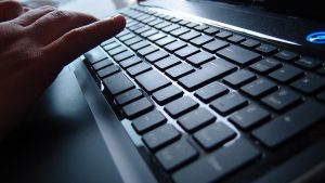 a hand hovers over a black keyboard with chicklet low-lift style keys, a brightly lit blue power button is visible in the upper corner