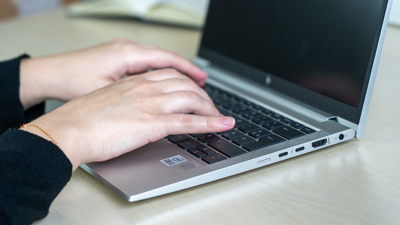 A pair of hands on a silver laptop sitting on a white table