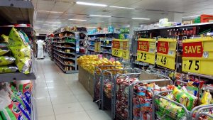A supermarket aisle with groceries and various signage visible of prices.