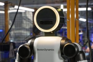 Boston Dynamics Atlas robot, standing, company name on silver chest, head is a black circle with a ring of yellow light surrounding it